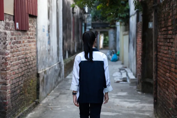 Huong porte un training bleu foncé avec des manches blanches. Elle marche dans une ruelle qui a l'air abandonnée.