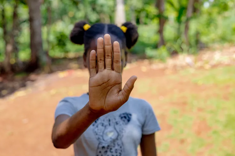 Teta fait "stop" de la main en montrant la paume de sa main à la caméra. Se faisant, elle cache son visage.